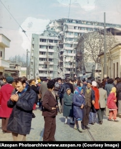 O mulțime de oameni se adună lângă un bloc de apartamente grav avariat în centrul Bucureștiului.