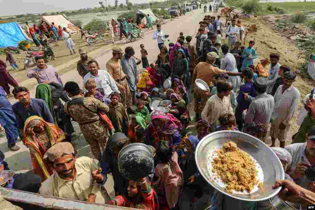 Personalul armatei pakistaneze distribuie alimente persoanelor afectate de inundații în apropierea unei tabere improvizate în urma ploilor musonice puternice din districtul Rajanpur din provincia Punjab, la 27 august 2022.
