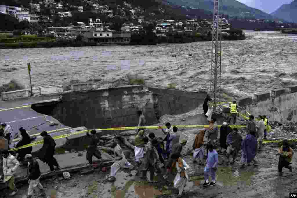 Oamenii se adună în fața unui drum afectat de inundații în urma ploilor musonice abundente în zona Madian din nordul Pakistanului, în Valea Swat, 27 august 2022. Mii de persoane care locuiesc în apropierea râurilor umflate de inundații din nordul Pakistanului au primit ordin de evacuare pe 27 august, în timp ce bilanțul victimelor ploilor musonice devastatoare depășește 1.000 de morți, fără a se întrevedea un sfârșit. Autoritatea națională de gestionare a dezastrelor din țară (NDMA) a declarat că 119 persoane au murit și 71 au fost rănite numai în ultimele 24 de ore. &nbsp;