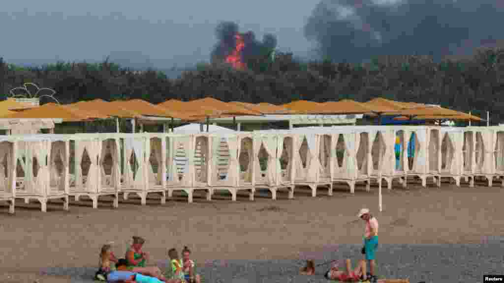 Néhányan még napoznak a strandon, miközben füst száll fel egy orosz katonai légi támaszpontról a 2014-ben megszállt Krím félszigeten 2022. augusztus 9-én