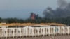 De pe o plajă la Marea Neagră, oamenii privesc fumul și flăcările după exploziile de la o bază aeriană militară rusă din Novofedorivka, Crimeea, în august 2022