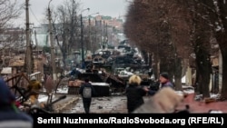 Civili posmatraju kolonu uništenih ruskih oklopnih vozila u Buči, u blizini Kijeva, 1. marta 2022. Taj grad su zauzele ruske trupe nekoliko dana nakon što je načinjena ova fotografija, ali su se povukle manje od mjesec dana kasnije.