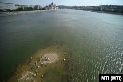 A csapadékhiány miatt alacsony a Duna vízállása, a Margitsziget déli csücske kiemelkedik a folyó vizéből a Margit híd alatt, Budapesten 2022. augusztus 6-án. Az ott lévő padon fiatalok ülnek