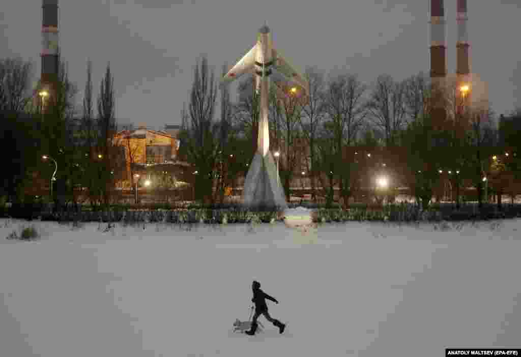 A Russian woman runs with a dog in front of a MiG-19 fighter plane, a monument to military pilots, in Aviators Park in St. Petersburg.&nbsp;