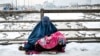 Авганистанка облечена во бурка седи со дете во скут на мост покриен со снег во Кабул. 