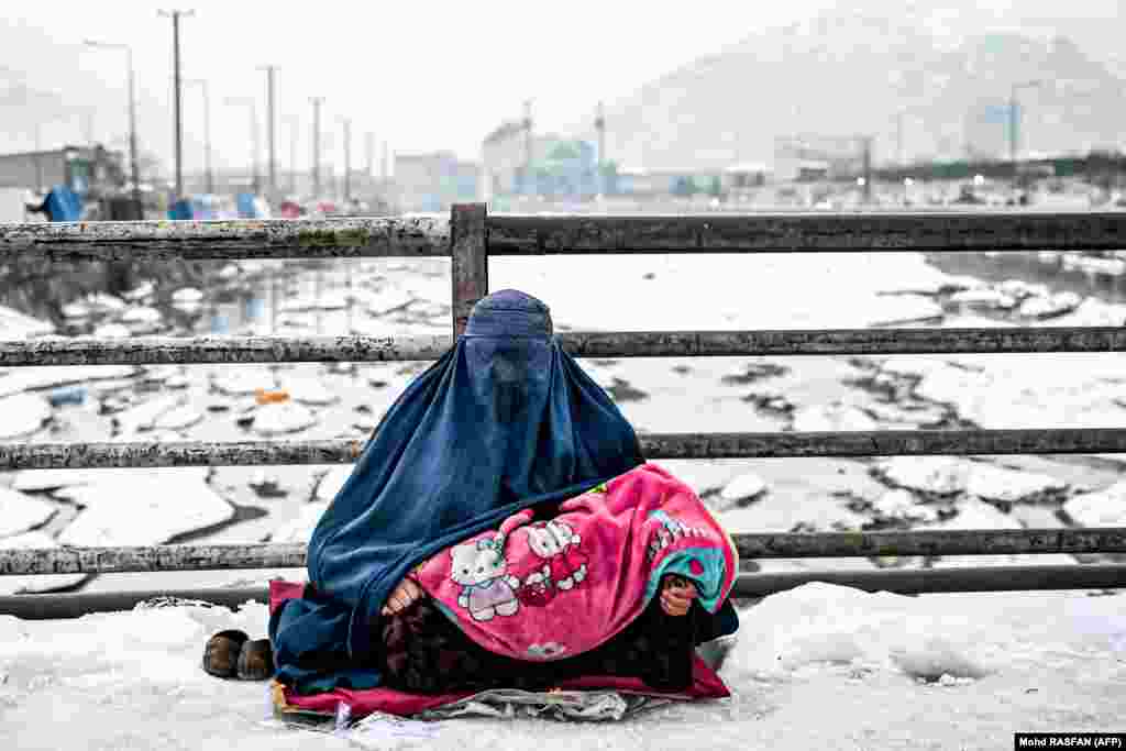 Një grua afgane e veshur me burka duke qëndruar e ulur në tokë, me fëmijën e saj në prehër, teksa kërkonte lëmoshë nga kalimtarët në një urë në Kabul, Afganistan, më 6 janar.