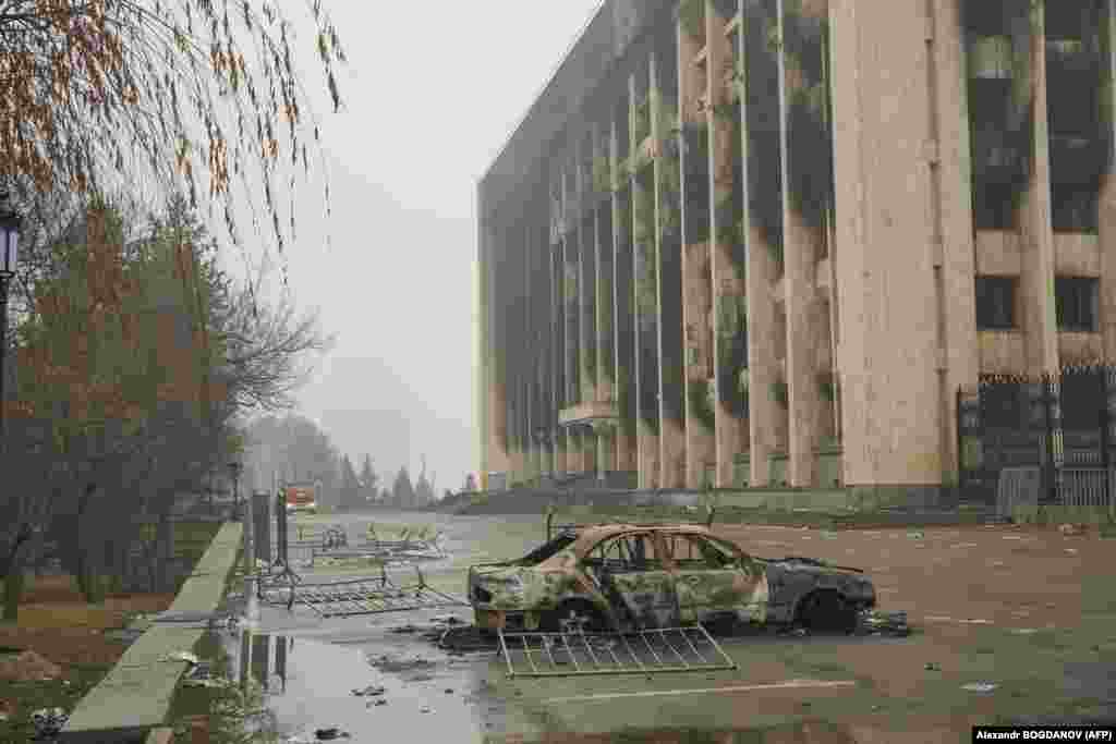 Një pamje e përgjithshme tregon një automjet të djegur para një ndërtese qeveritare, po ashtu, të djegur në qendër të Almatit, më 7 janar 2022.