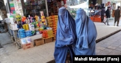 Afghan women, wearing burqas, walk down a market street in Kabul.