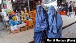 Afghan women wearing burqas walk down a market street in Kabul.
