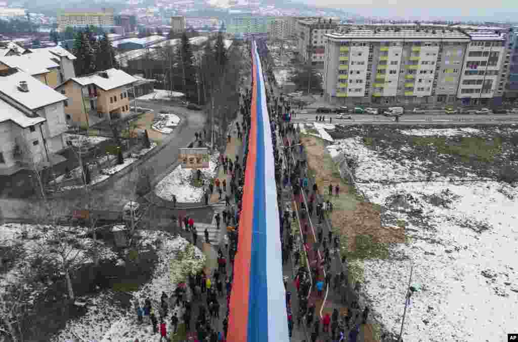 Bosnian Serbs march carrying a giant Serbian flag in Sarajevo on January 9 to celebrate an outlawed holiday with a provocative parade showcasing armored vehicles, police helicopters, and police officers with rifles, marching in lockstep and singing a nationalist song.