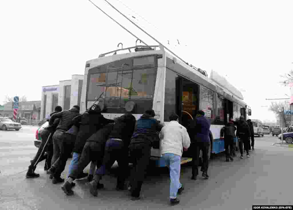 People help to push a trolley bus from an intersection during a power outage in the Kyrgyz capital, Bishkek, on January 25.&nbsp;