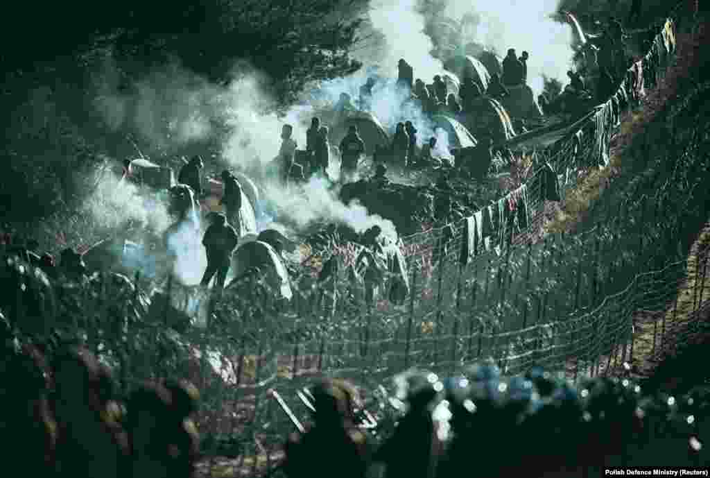 A photo taken in November 2021 shows migrants along the edge of Belarusian territory, with Polish servicemen massed on the EU side in the foreground. Scenes like this came after thousands of mostly Middle Eastern migrants were allegedly lured to Belarus, then ferried toward the borders with EU countries. The 2021 migrant crisis came after EU sanctions were imposed against Belarus in the wake of postelection violence and the seizure of a Ryanair passenger jet by the regime of President Alyaksandr Lukashenka.