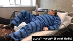 تصویری از بکتاش آبتین با لباس زندان و پابند بر تخت بیمارستان