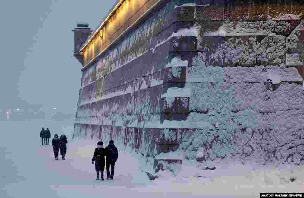 People walk along the wall of the Peter and Paul Fortress during a snowfall in St. Petersburg, Russia.