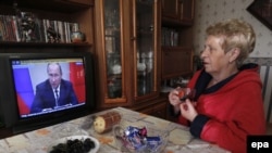 A woman watches a TV showing Russian President Vladimir Putin making a statement at a cabinet meeting at his residence outside Moscow on September 30.
