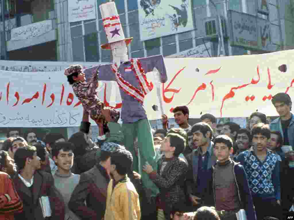 Iran -- An effigy of US President Carter during a demonstration outside of the US Embassy in Tehran, 18Nov1979 - IRAN, Tehran : Boy in camouflage fatigues points toy pistol at an effigy of U.S. President Carter topped with empty cartoons of American-made Winston cigarettes boycotted by Iranians in the current campaign against the United States, during a demonstration outside of the U.S. Embassy, 18 November 1979