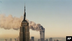 Turnurile gemene de la World Trade Center arzînd în spatele blocului Empire State Building, New York, 11 septembrie 2001.