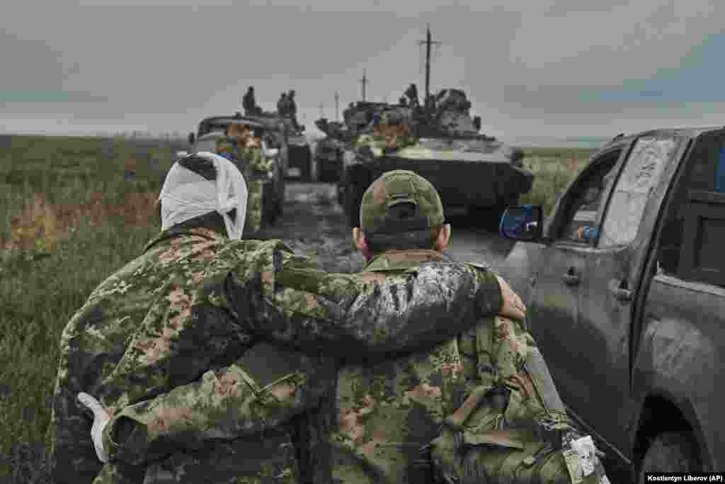 Украінскі вайсковец дапамагае параненаму аднапалчаніну на дарозе на вызваленай тэрыторыі ў Харкаўскай вобласьці Ўкраіны.