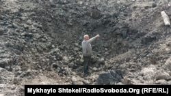 Человек стоит в воронке от, вероятно, авиабомбы в Николаевской области. Украина, архивное фото