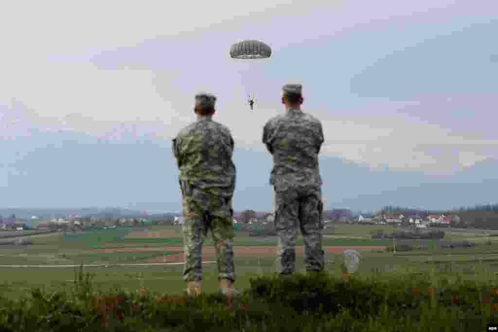 Two soldiers watch as U.S. troops conduct parachute training exercises to keep soldier's skills fresh at Camp Bondsteel in Kosovo. (epa/Valdrin Xhemaj)