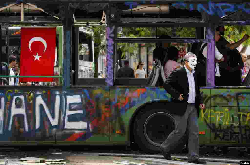 Hökümete garşy çykýan protestçi Taksim meýdançasynda böwet hökmünde ulanylan, ýanan bir awtobusyň golaýyndan geçip barýar. 5-nji iýun