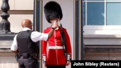 Un polițist dă apă unui soldat din Garda Regală la palatul Buckingam din Londra. 