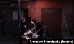 Doi locuitori din Mariupol gătind în curtea blocului în vara anului 2022.
