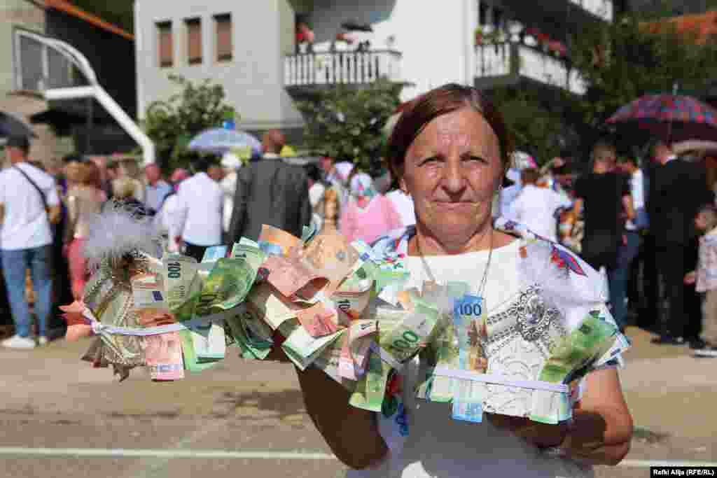 Një grua mban tri kapela rreth së cilave janë vendosur paratë dhuratë për fëmijët/djemtë që i janë nënshtruar aktit të synetimit.&nbsp;&nbsp;&nbsp; Secila familje ndan një shumë të caktuar parash, pavarësisht nëse kishte fëmijë për t&#39;u bërë synet. Festimi sivjet kushtoi rreth 30.000 euro.
