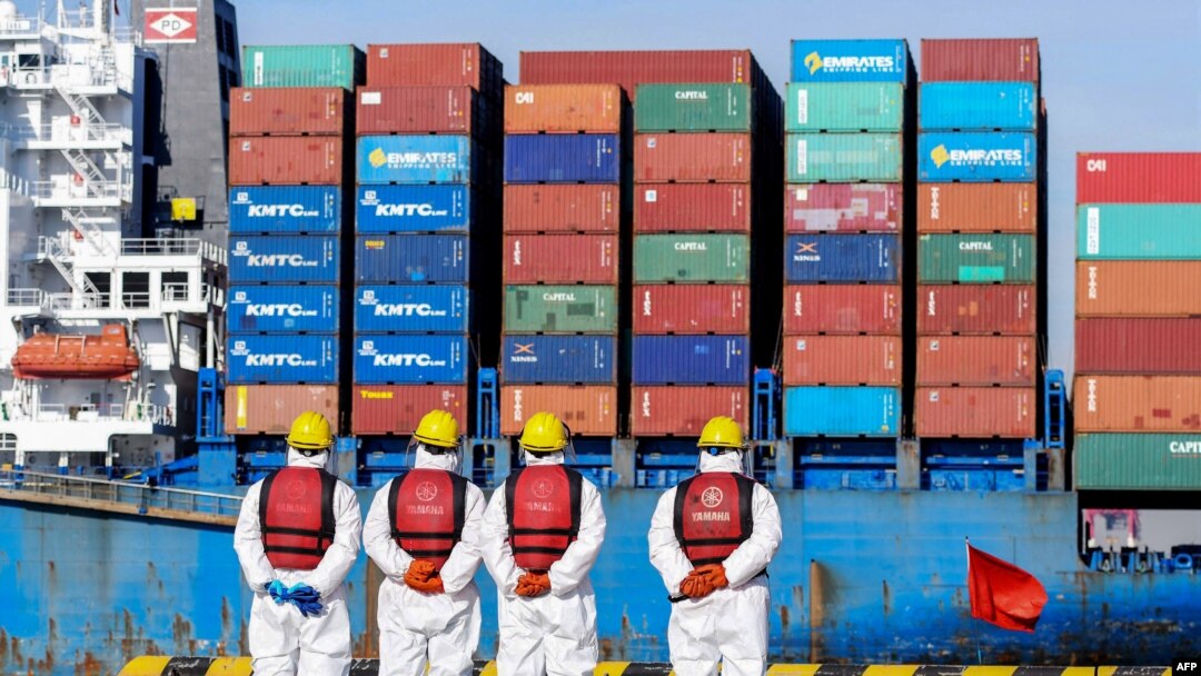 Angajați purtând echipamente de protecție personală (PPE) privesc o navă de marfă într-un port din Qingdao, în provincia chineză Shandong, la 14 ianuarie 2022.