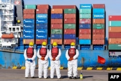 Muncitori din China în fața unei nave de marfă în portul din Qingdao. Relațiile comerciale SUA-China au devenit tot mai reci în ultimii ani