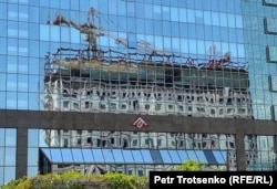 Отражение строящегося жилого дома в стеклянных стенах бизнес-центра «Нурлы-тау». Алматы, 18 июля 2022 года