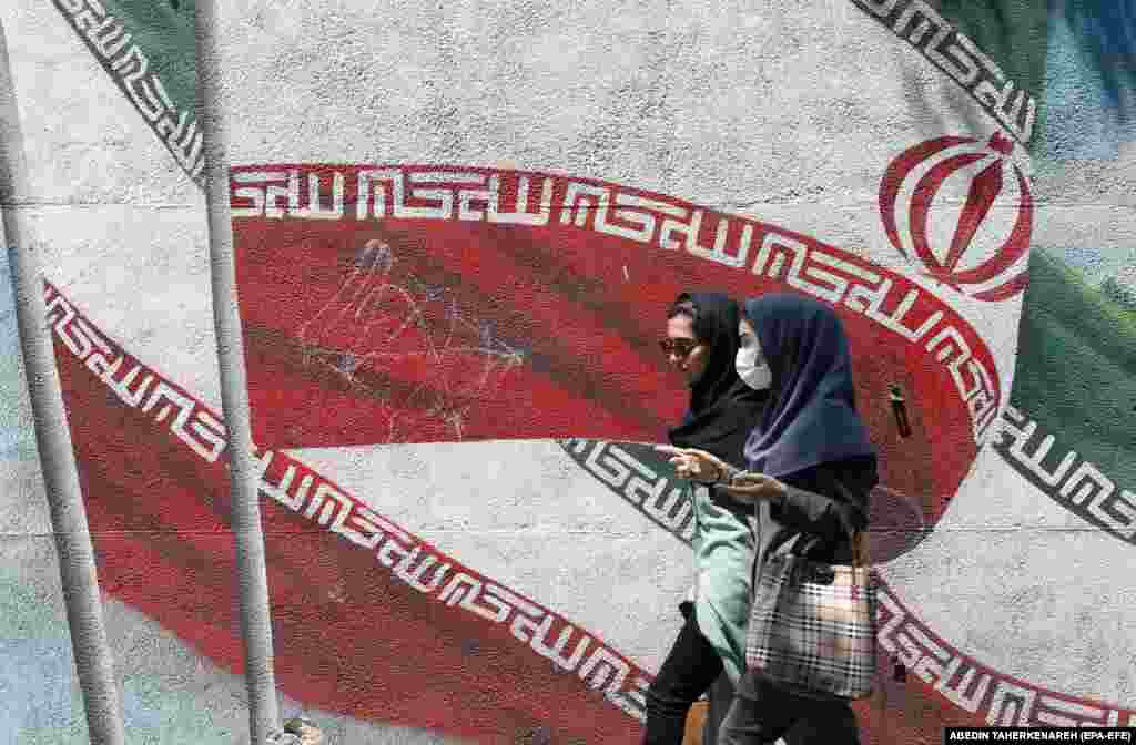 Iranian women walk past a mural of Iran&rsquo;s national flag on a street in downtown Tehran.