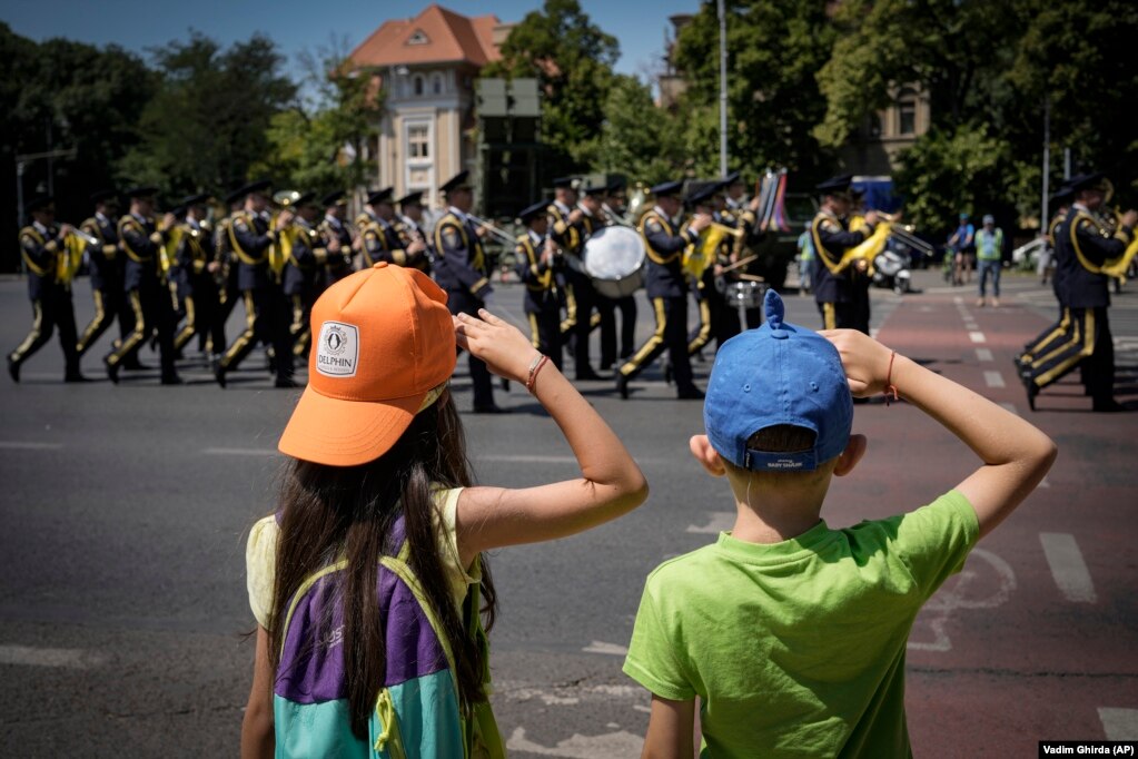 Deca razigrano pozdravljaju vojni orkestar na kraju ceremonije kod spomenika herojima avijacije u Bukureštu 20. jula.