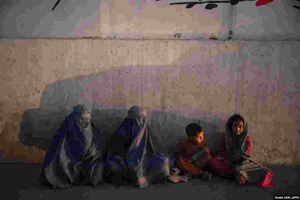 Burqa-clad Afghan women sit with children on the side of a Kabul street.