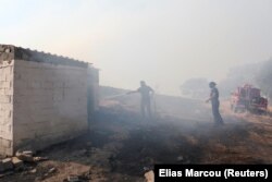 Un localnic stropește cu apă un incendiu de vegetație care arde în apropierea satului Vatera, pe insula Lesbos, Grecia, 24 iulie 2022.