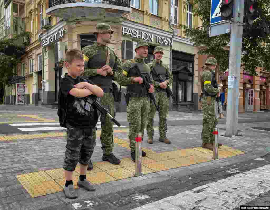A boy with a toy rifle stands next to Ukrainian fighters in central Kyiv on June 22.&nbsp;
