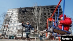 Діти в окупованому Маріуполі граються перед будівлею, яка була пошкоджена під час бойових дій в березні 2022 року