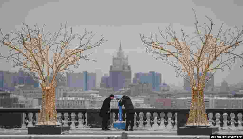 Two men look at Moscow buildings through a telescope at the Vorobyovy Gory&nbsp;observation deck in the Russian capital.&nbsp;