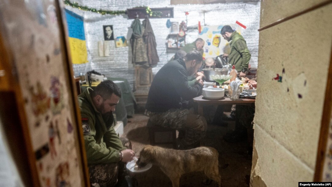 A Ukrainian soldier feeds his dog as other soldiers eat in a shelter at a frontline position amid a buildup of Russian troops near Ukraine. The U.S. State Department has warned Americans to leave Ukraine as tensions surge in the region.