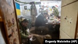 A Ukrainian soldier feeds his dog as other soldiers eat in a shelter at a frontline position amid a buildup of Russian troops near Ukraine. The U.S. State Department has warned Americans to leave Ukraine as tensions surge in the region.