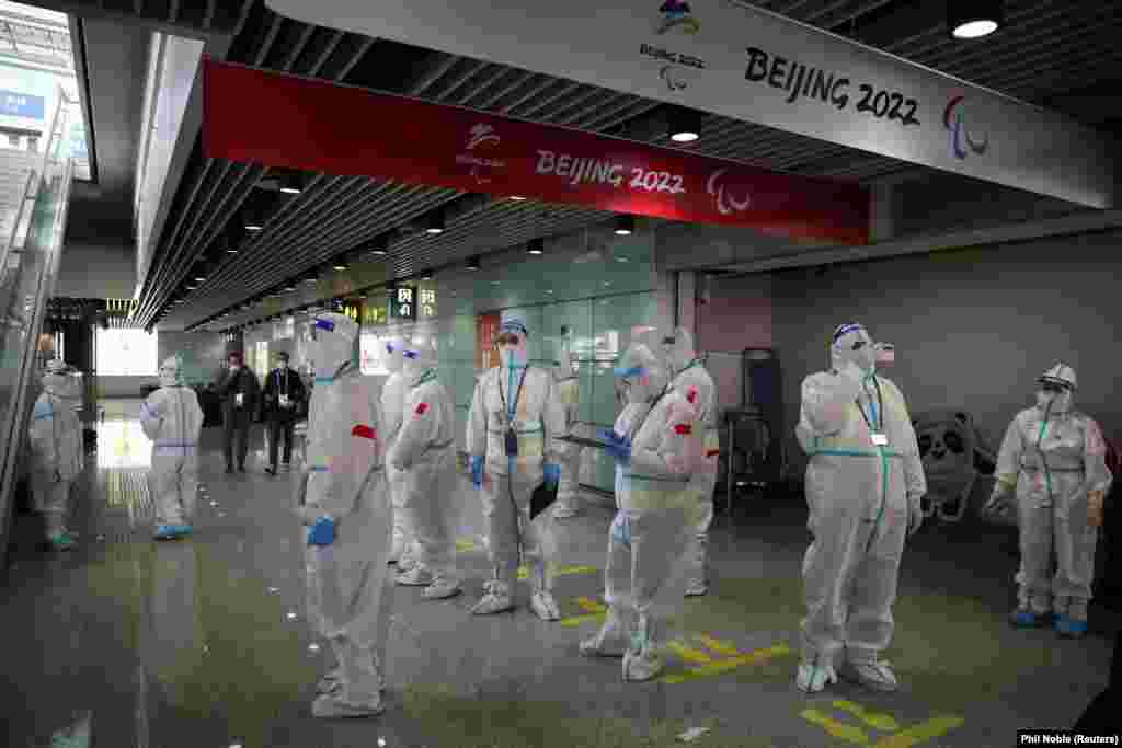 Teljes védőfelszerelésbe bújt személyzet várja a téli olimpiára érkező sportolókat a pekingi repülőtéren január 31-én