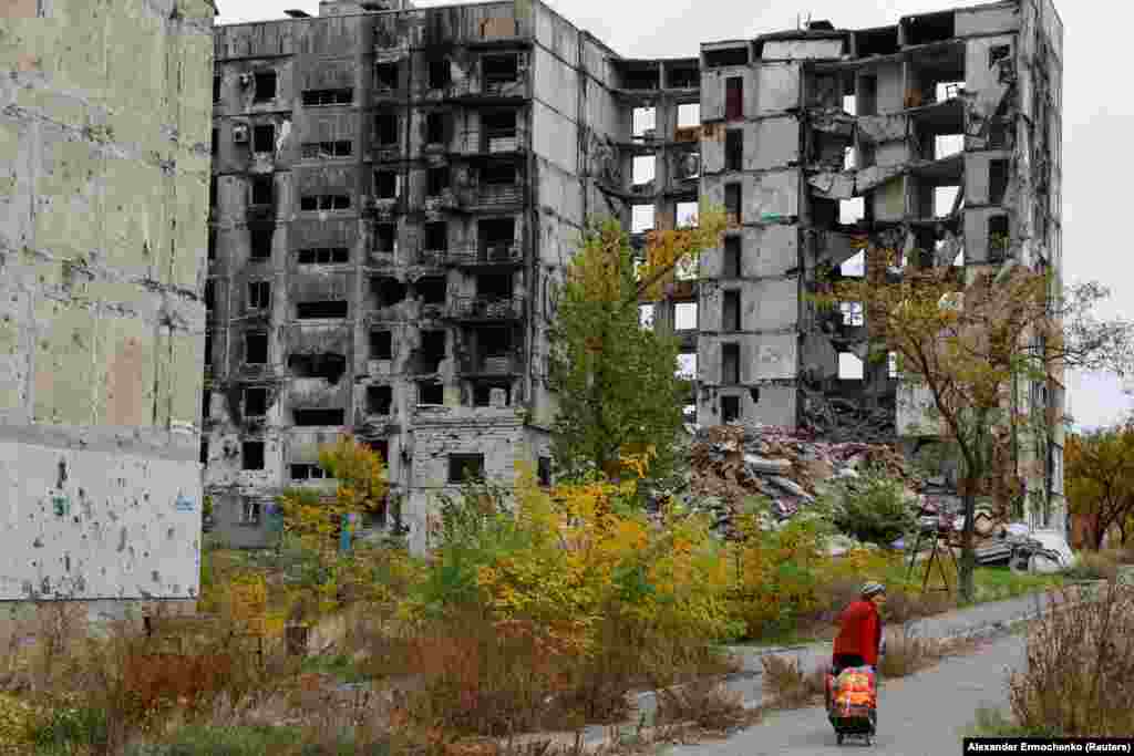 A woman walks past a ruined apartment building on October 29.&nbsp;