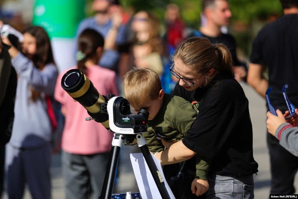Një fëmijë i vogël shikon në pajisjen optike eklipsin e Diellit.