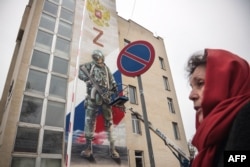 O femei din Rusia trece pe lângă o clădire pe care este desenată un soldat rus, împreună cu simbolul „Z”, asociat în Rusia cu susținerea pentru invazia Ucrainei.