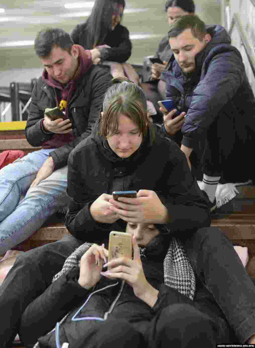 Люди смотрят на экраны смратфонов, укрывшись на станции метро в Киеве во время российского ракетного удара. 31 октября 2022 года
