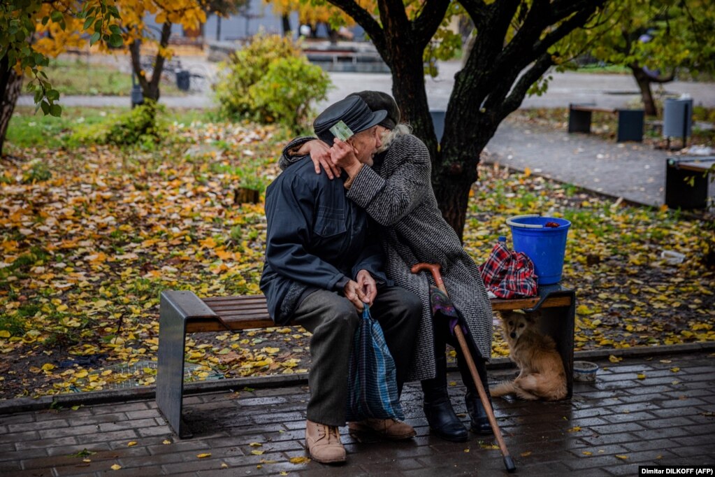 Një çift të moshuarish duke u përqafuar. Të moshuarit janë ulur në një stol në qytetin e vijës së parë të Bahmutit gjatë një momenti qetësie nga bombardimet më 27 tetor 2022. Rajoni lindor i Ukrainës është sulmuar nga forcat ruse prej muajsh.
