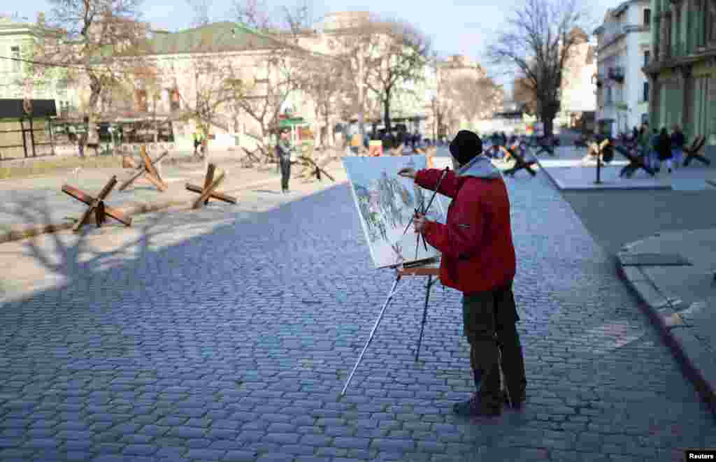 Pictorul Viktor Olîinik, în vârstă de 67 de ani, pictează un peisaj urban cu bariere antitanc pe străzile din Odesa, Ucraina, în luna martie 2022.