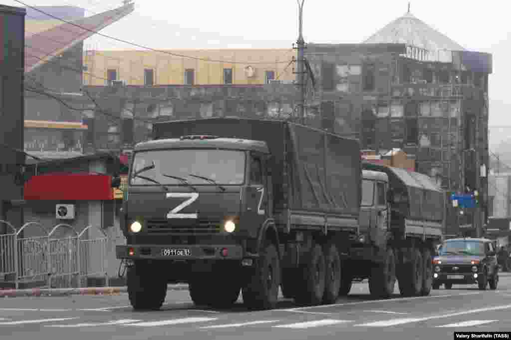 Oktâbrniñ 19-nda yapılğan fotoresimde Mariupol merkezindeki zarar körgen bina ögünde Rusiye arbiy yük maşinaları köründi.