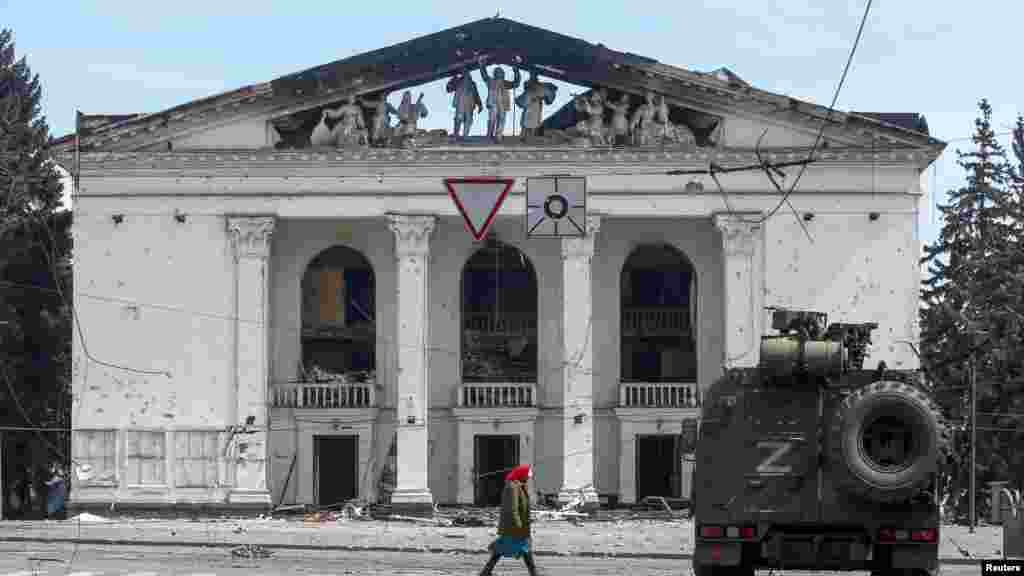 An elderly woman walks past the destroyed theater and an armored vehicle of pro-Russian forces in April 2022.&nbsp;