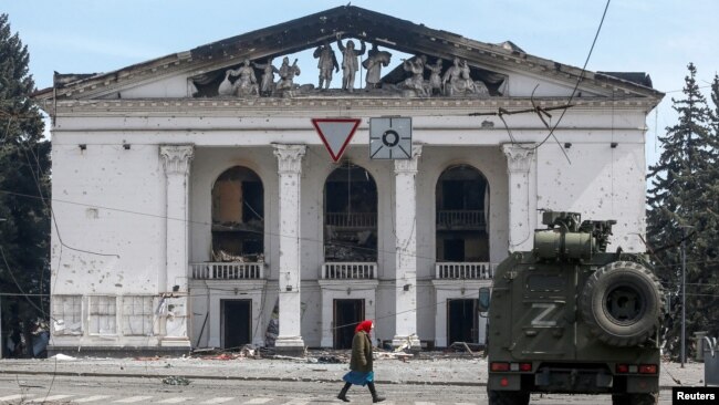 A woman walks next to an armored vehicle manned by pro-Russian troops outside the desroyed Donetsk Academic Regional Drama Theater in Mariupol on April 10.